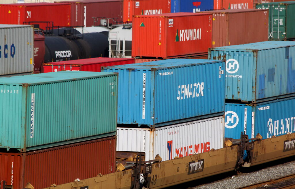 Colourful shipping containers stacked at a rail freight yard, representing cross-border trade