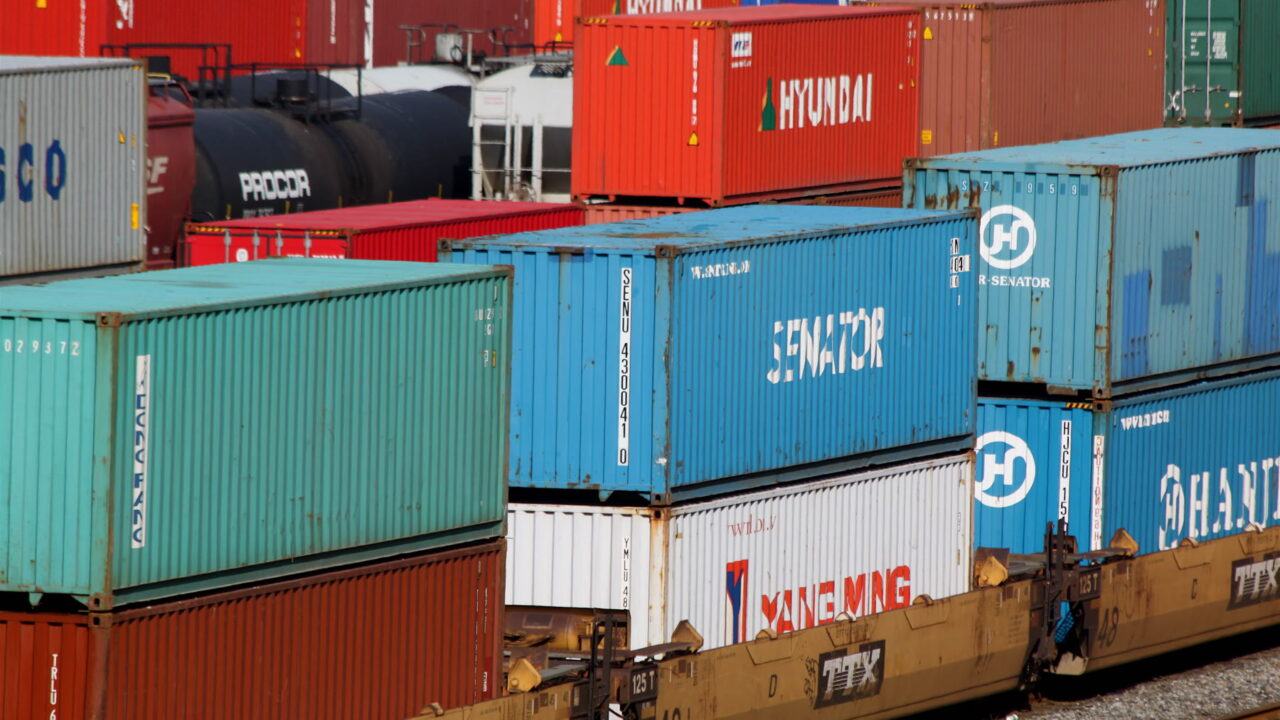 Colourful shipping containers stacked at a rail freight yard, representing cross-border trade