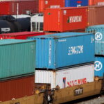 Colourful shipping containers stacked at a rail freight yard, representing cross-border trade